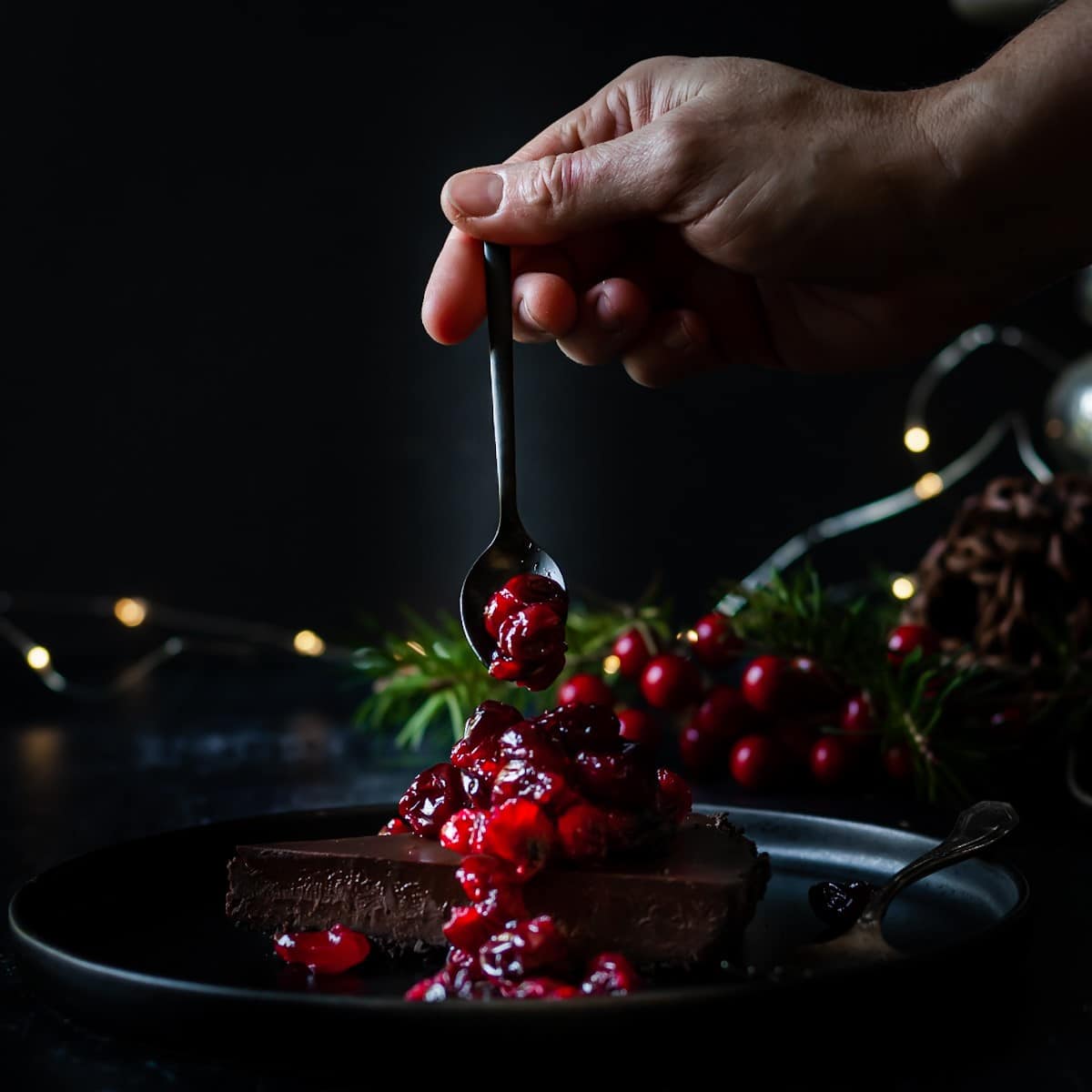 slice of chocolate tart with cranberries and cranberries being spooned onto the tart