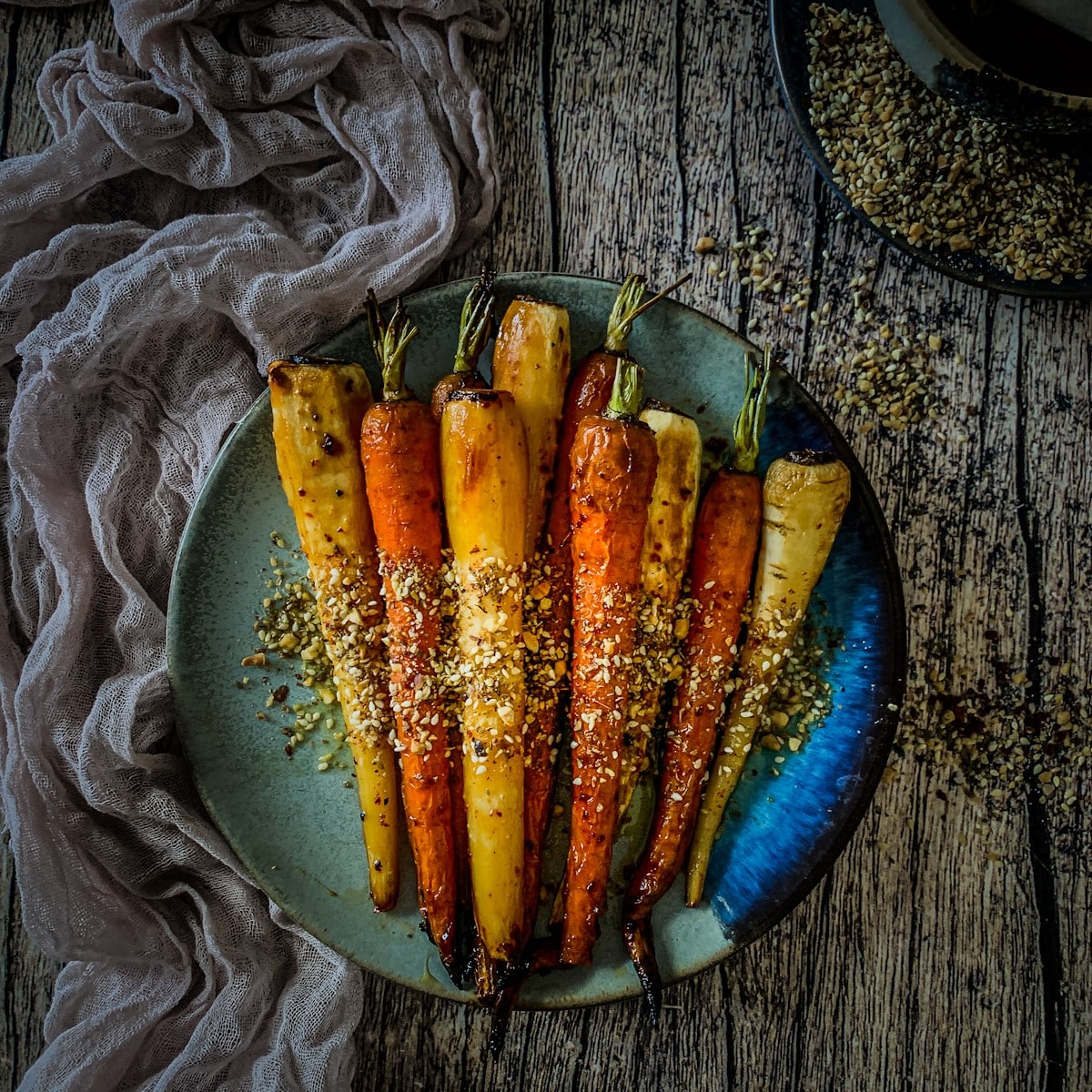 Overhead view of honey roasted carrots and parsnips with dukkah on a blue plate.