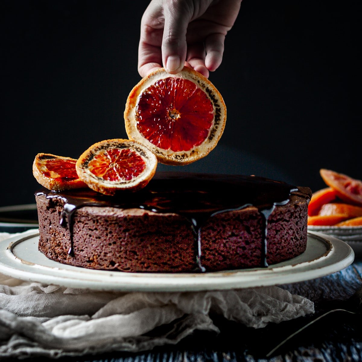 Blood orange being placed on a boozy chocolate cake.