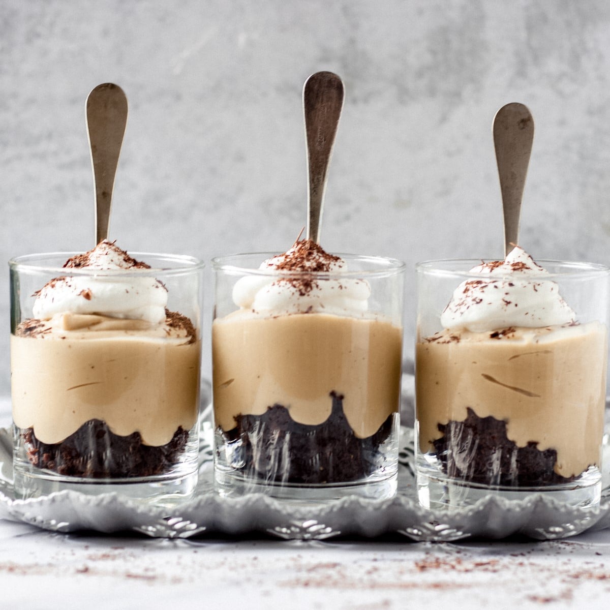 Three glasses of butterscotch budino with spoons in them.