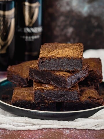 Guinness stout chocolate brownies stacked on a plate in front of guinness beer cans.