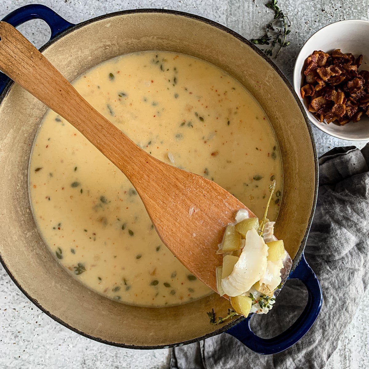 Flaked fish on a wooden spoon over a pot of seafood chowder.