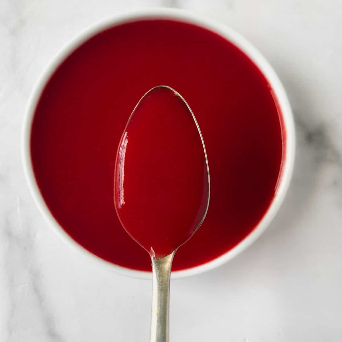 Spoon with strawberry coulis over a bowl.
