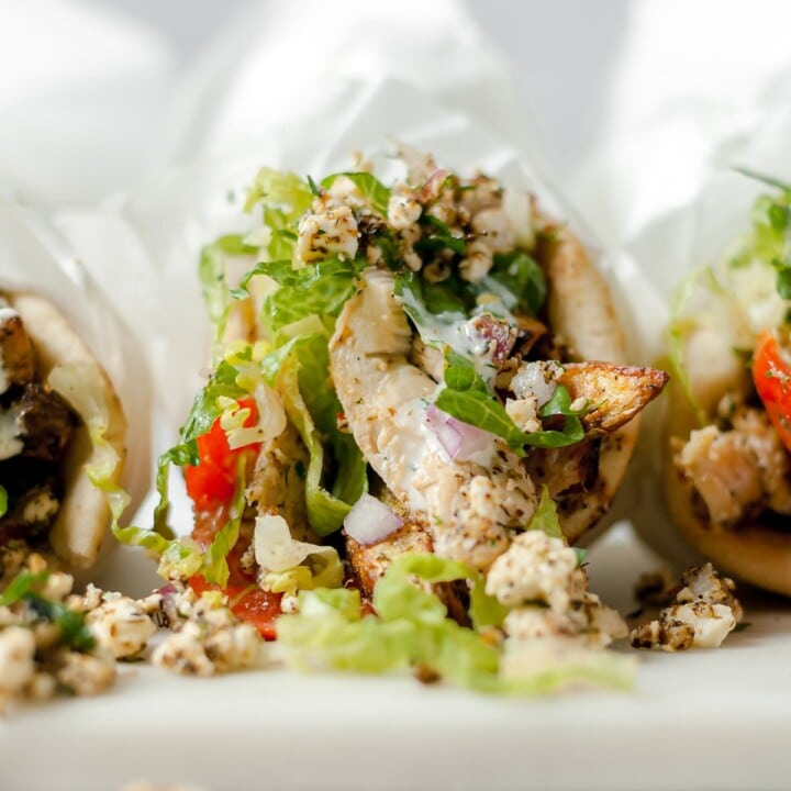 Closeup of chicken pita wrapped in parchment with lettuce, tomato, onion and feta cheese.