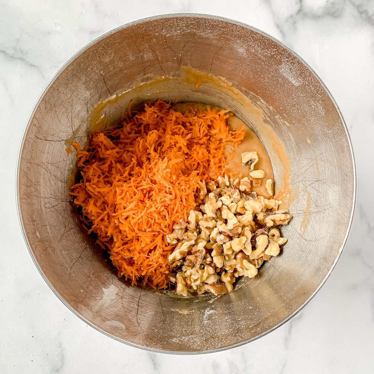 Carrots and walnuts in cake batter in a metal bowl.