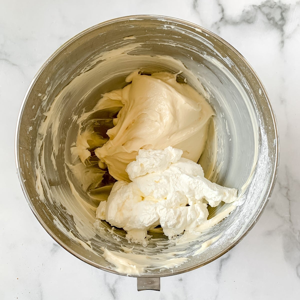 Cream cheese frosting and whipped cream in a metal bowl.