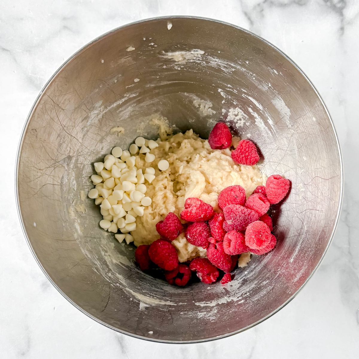 Overhead shot of muffin batter with raspberries and white chocolate.